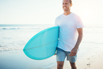 Young guy surfer walking with surfboard near the ocean