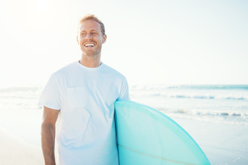 Smiling guy surfer walking with surfboard near the ocean