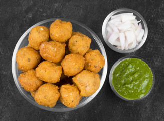 Indian Spicy Street Food Dal Vada Also Know as Moong Dal Vada, Pakoda, Pakode, Pakore, Moong Vada, Pakora or Bhajiya Served with Green Chutney or Onion on Black Background
