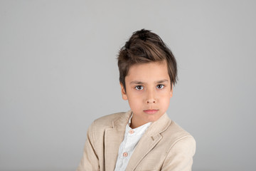 Waist up portrait of an attractive brunette boy in a beige jacket on a gray background in the studio
