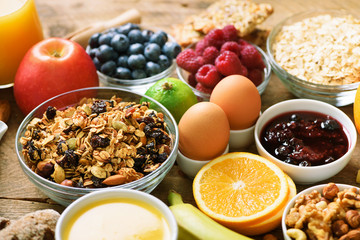 Healthy breakfast ingredients, food frame. Granola, egg, nuts, fruits, berries, toast, milk, yogurt, orange juice, cheese, banana, apple on wooden rustic background, top view, copy space.