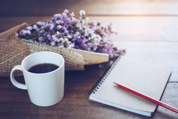 a cup of black coffee and open book blank page with flowers on wooden table