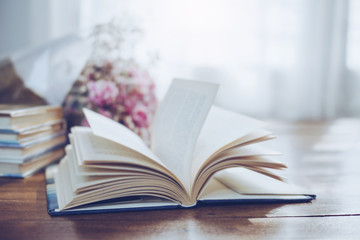 flying and blurred open page of old book with flowers on wooden background