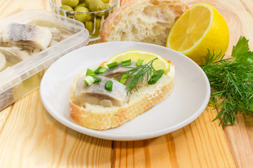 Open sandwich with pickled herring among ingredients for its preparation