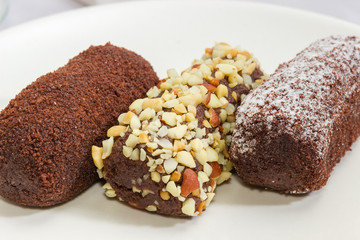 Three chocolate pastries with different sprinklings on white dish closeup