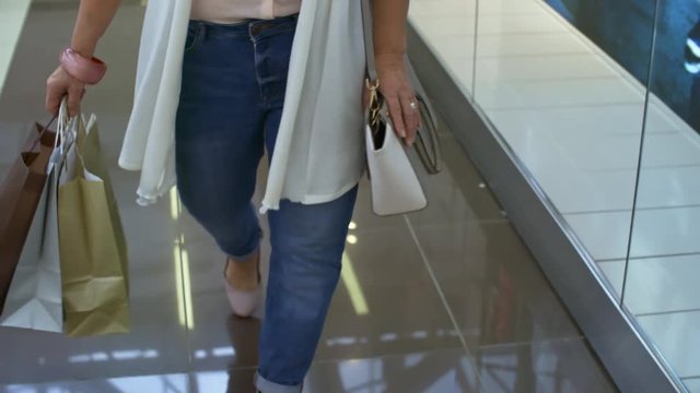 Legs of unrecognizable stylish woman carrying paper bags with purchases after buying clothes in shopping center