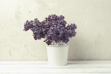 White Decorative Pail Bucket with Lilac on a white stone background and white wooden table. Flat lay, top view