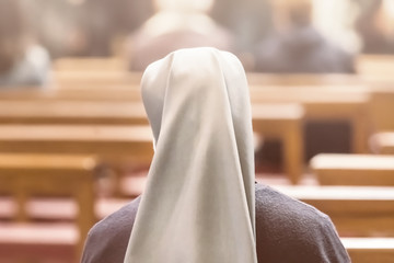 A nun is sitting on a bench during a church service, the view from the back