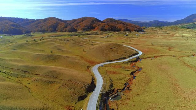 Aerial over autumn valley with flat hills and twisty paved road