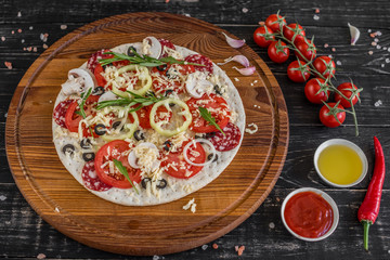 Vegetables, mushrooms and tomatoes pizza on a black wooden background. It can be used as a background
