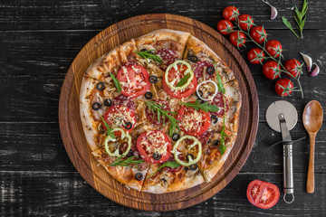 Vegetables, mushrooms and tomatoes pizza on a black wooden background. It can be used as a background