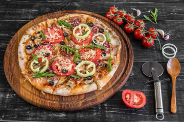 Vegetables, mushrooms and tomatoes pizza on a black wooden background. It can be used as a background