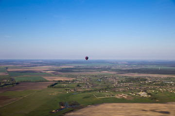 flying in a balloon over the flat natural landscape of the countryside of central Ukraine: fields, forests and lakes on a sunny morning against the blue sky