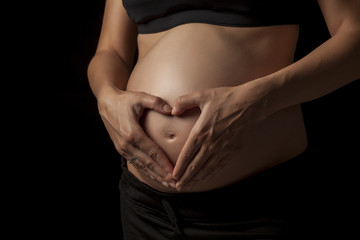 belly of a pregnant woman with hands on dark background