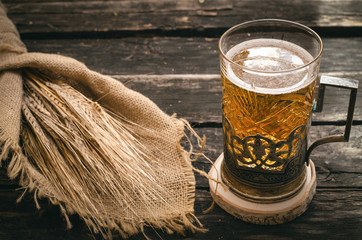 Glass of light beer and rye ears wrapped in burlap cloth on aged wooden background. Cold alcohol.