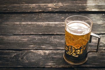 Glass of frothy light beer on the wooden table on aged wooden background.