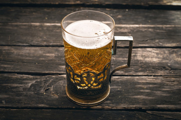 Glass of frothy light beer on the wooden table on aged wooden background.