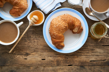 Fresh croissant, a cup of coffee and honey on a wooden table       