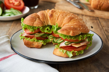 Croissant sandwich with tomatoes, cucumbers, bacon, cheese and lettuce on a plate