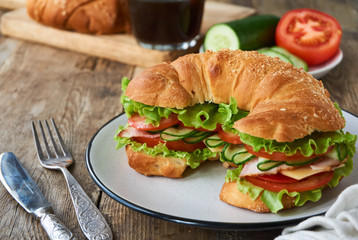 Croissant sandwich with tomatoes, cucumbers, bacon, cheese and lettuce on a plate