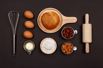 Fototapeta na wymiar Homemade breads ingredients, flour, almond nuts, hazelnuts, eggs on dark background, Cooking breakfast concept. Flat lay, Top view.