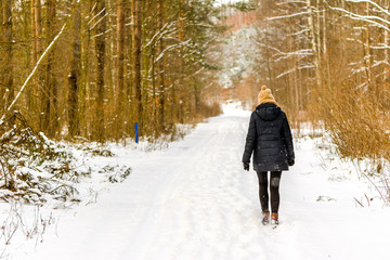 Depressed woman walking in snow in winter warm clothes, back view