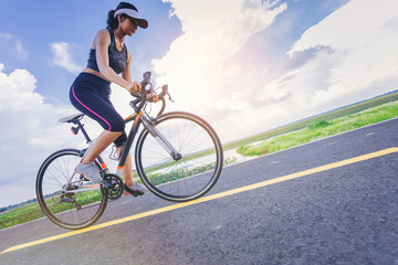 Fototapeta na wymiar Sporty girl cyclist riding sprint bicycle along the bike lane with cloudy sky as background