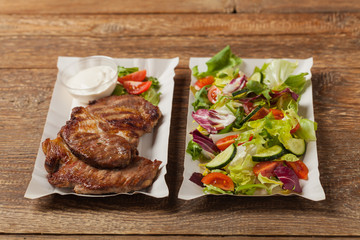 Grilled pork neck served on paper trays.