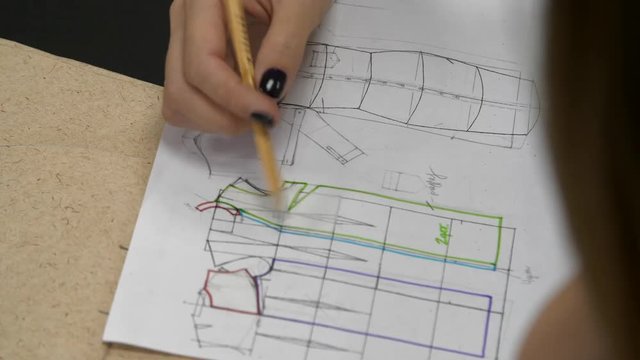 A girl raises a sketch of clothes, draws a sketch on paper
