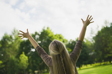 female teen girl from behind standing in park with raised arms