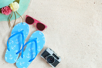 Beach background.  Top view of beach sand with straw hat, sunglasses, slippers and camera.  Summer background concept.