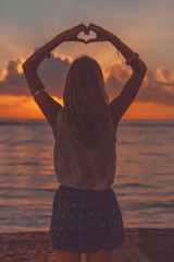 Girl holding heart shape in the sunset / sunrise time.