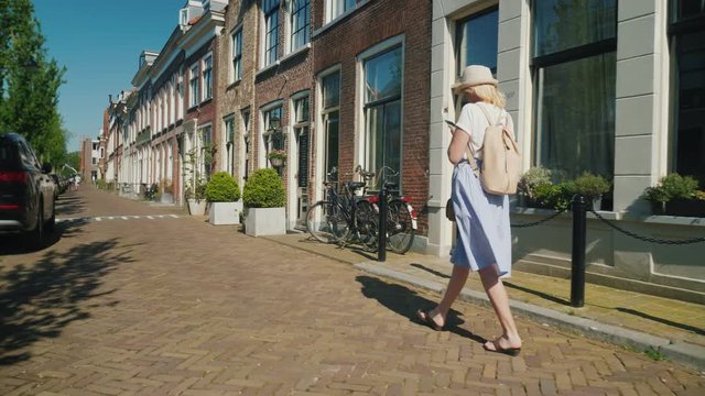 A tourist with a smartphone is walking along a deserted narrow street in the old European city of Delft. Travel to the Netherlands and Europe. Rear view