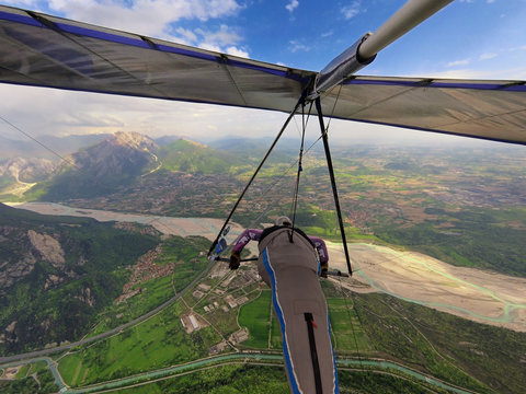 Brave extreme hang glider pilot flies high over valley with river and mountains