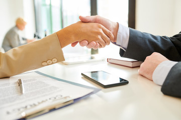 Side view close up of unrecognizable female manager shaking hands with client over contract lying on table after negotiations during meeting in office