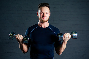 Fototapeta na wymiar young and handsome athlete man doing exercises for the muscles of the hands of dumbells in the gym. Crossfit and concept of health