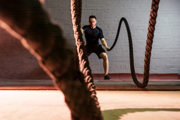 young and handsome male athlete man doing exercises for the muscles of the body with a battle ropes...