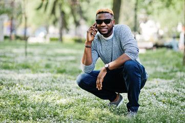 Stylish african american boy on gray sweater and black sunglasses posed on park and speaking on...