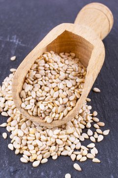 Sesame seeds in a wooden scoop on a dark granite stone background 