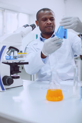 Being a researcher. Clever experienced biologist working with his microscope and holding a tube
