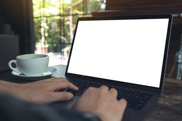 Mockup image of hand using laptop with blank white desktop screen with coffee cup on wooden table in cafe