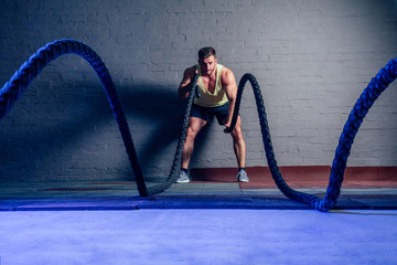 young and handsome male athlete man doing exercises for the muscles of the body with a battle ropes ( rope ) in fitness gym. concept of a healthy lifestyle and crossfit
