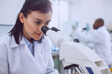 I feel happy. Content smart scientist working with her microscope and wearing a uniform