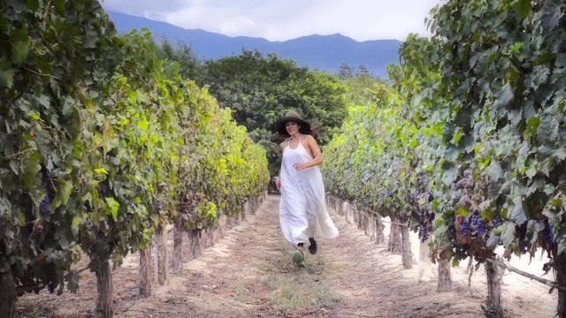 Brunette woman running away from the vineyards wearing a bride dress, Slow motion