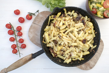 Home-made fried potatoes in an old frying pan and vegetable salad located on a light background