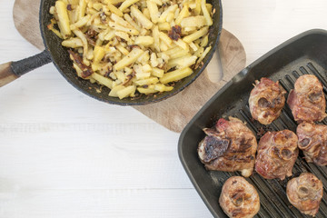 Fried homemade potatoes and grilled meat frying pan on a light wooden background