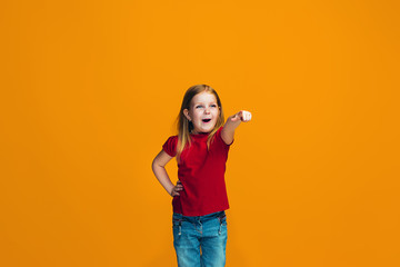 The happy teen girl pointing to you, half length closeup portrait on orange background.