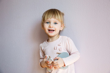 Happy little girl. A little girl with blond hair holds two wooden white hearts in her hands, looks at the viewer and laughs.