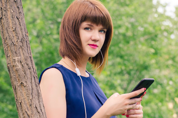 Beautiful young girl in summer weather listening to music on headphones outdoors, on a green glade