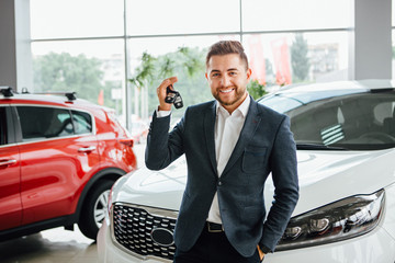 Man is holding a key of their new car, looking at camera and smiling.